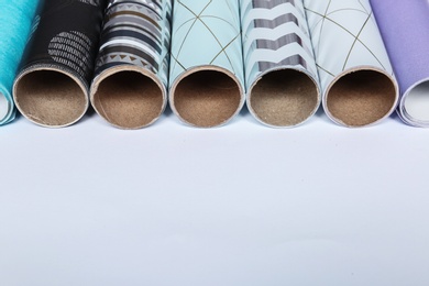 Rolls of festive wrapping paper and space for text on white background, closeup. Gift box packaging ideas