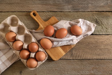 Photo of Raw chicken eggs with carton, napkin and board on wooden table, flat lay