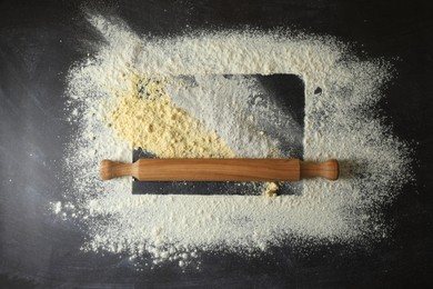 Photo of Flour and rolling pin on black table, top view