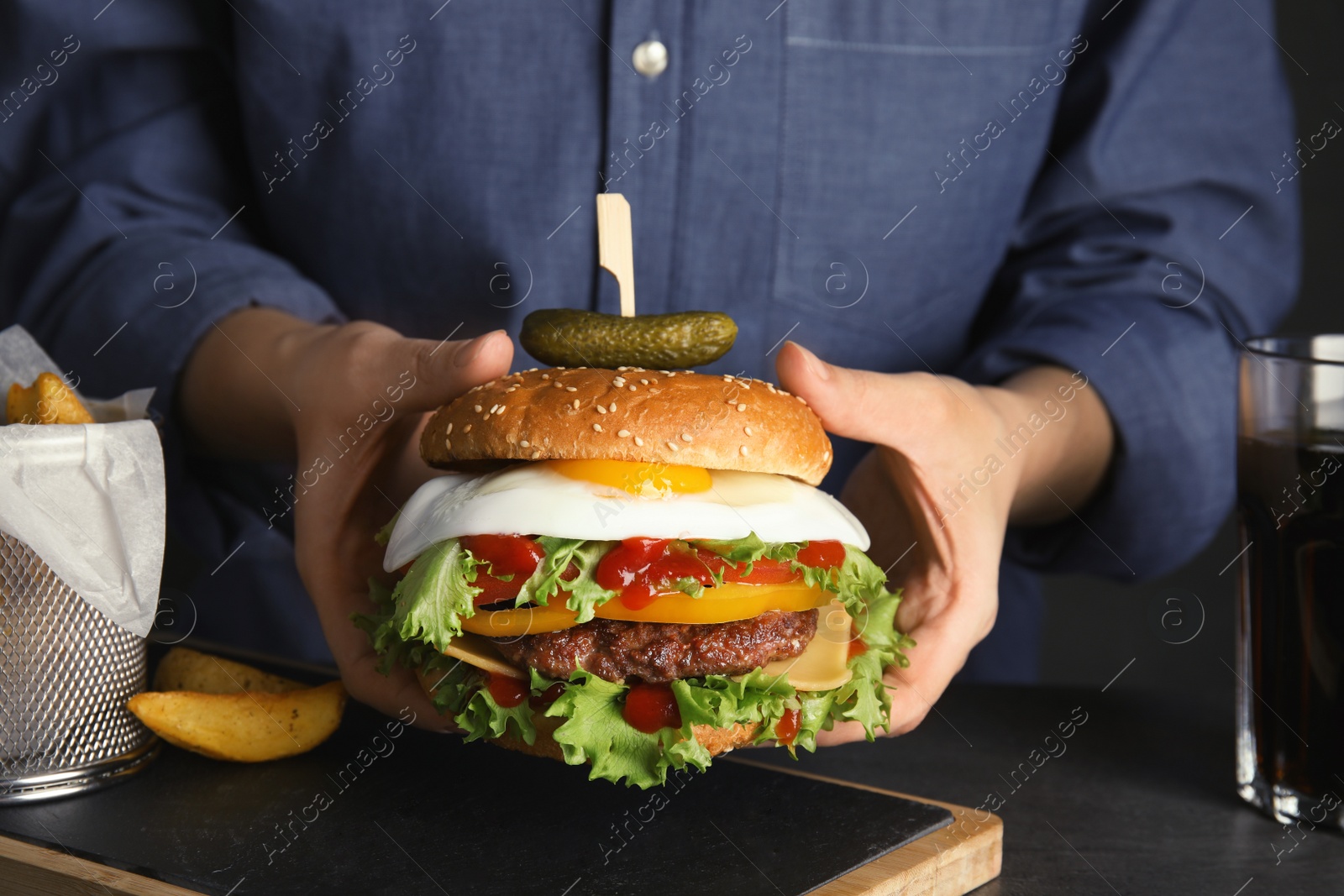 Photo of Woman holding tasty burger with fried egg over table, closeup