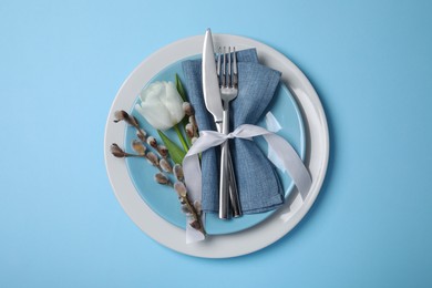 Festive table setting with willow twigs and tulip on light blue background, top view. Easter celebration