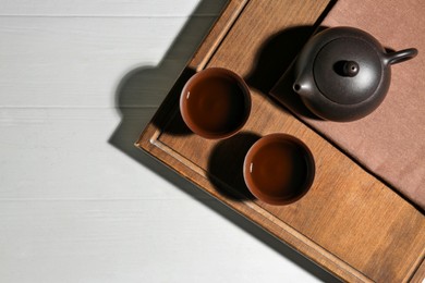 Photo of Cups of aromatic tea and teapot on white wooden table, top view. Space for text