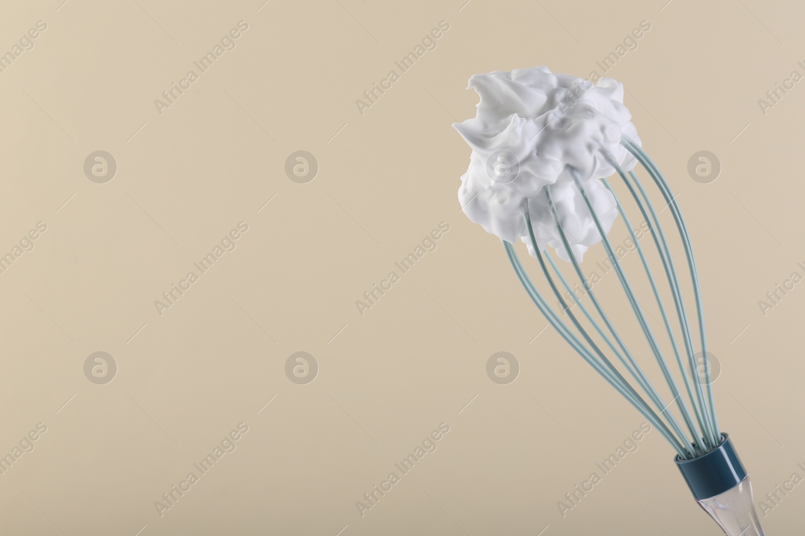 Photo of Whisk with whipped cream on beige background. Space for text