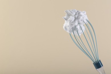 Photo of Whisk with whipped cream on beige background. Space for text