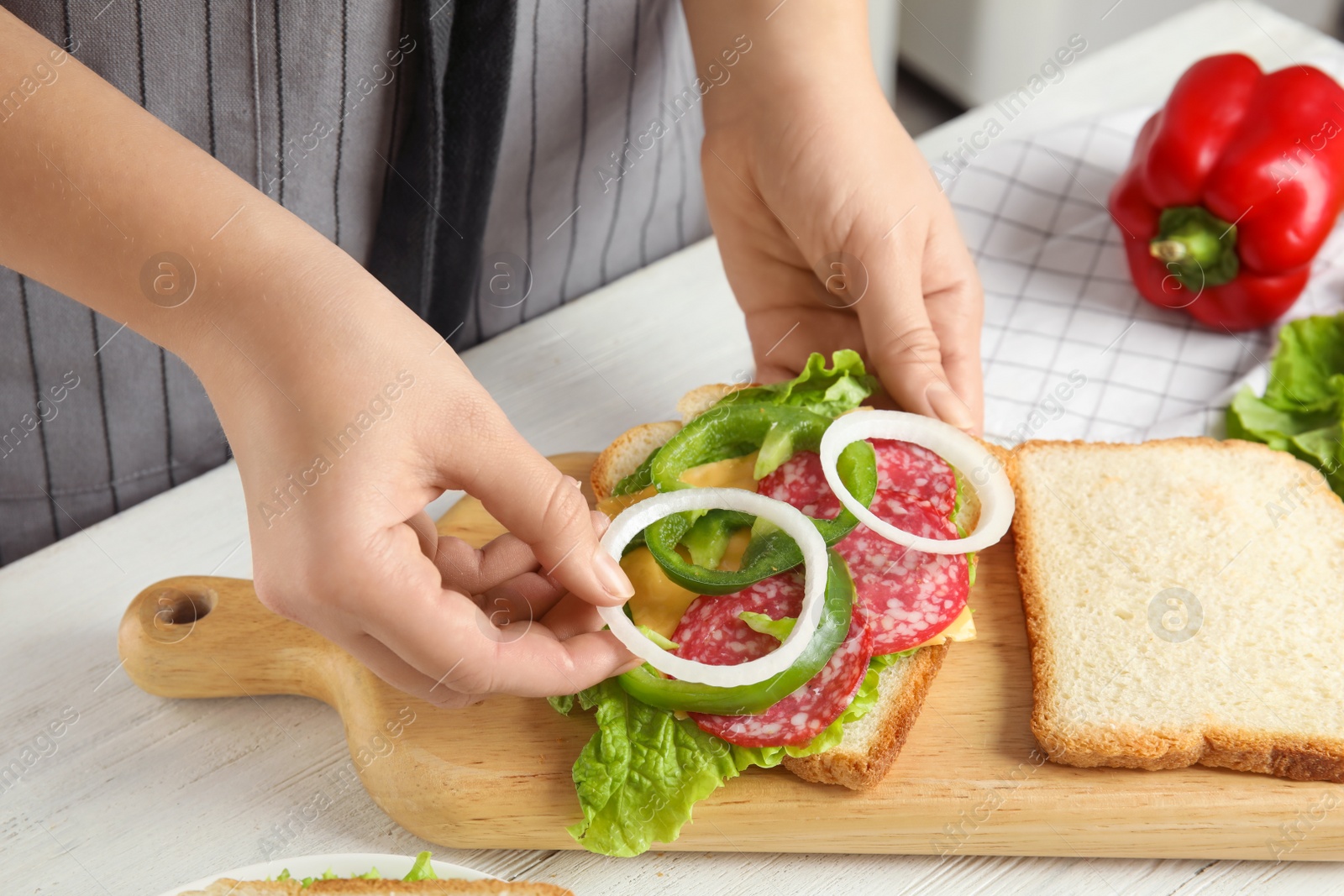 Photo of Woman adding onion to tasty sandwich at white wooden table, closeup