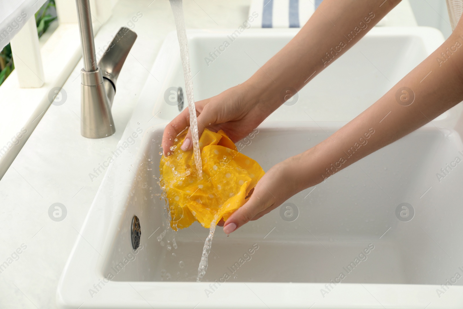 Photo of Woman washing beeswax food wrap under tap water in kitchen sink, closeup