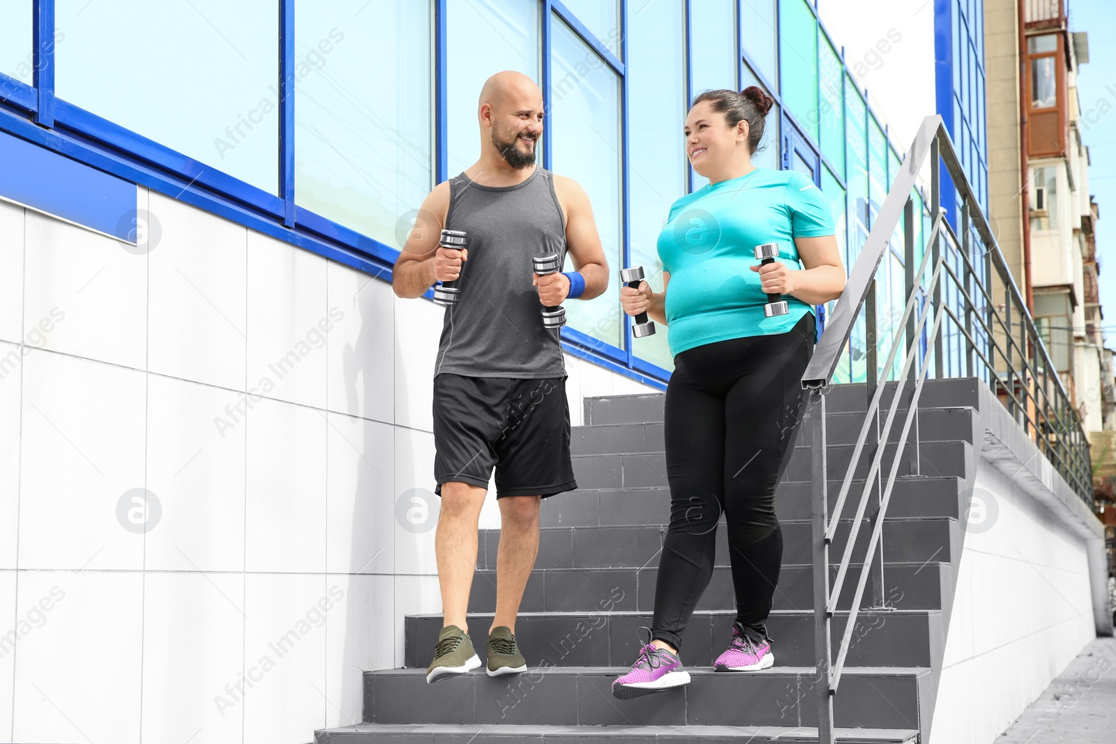 Photo of Overweight man and woman running with dumbbells on stairs outdoors