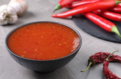 Photo of Spicy chili sauce in bowl and peppers on grey table