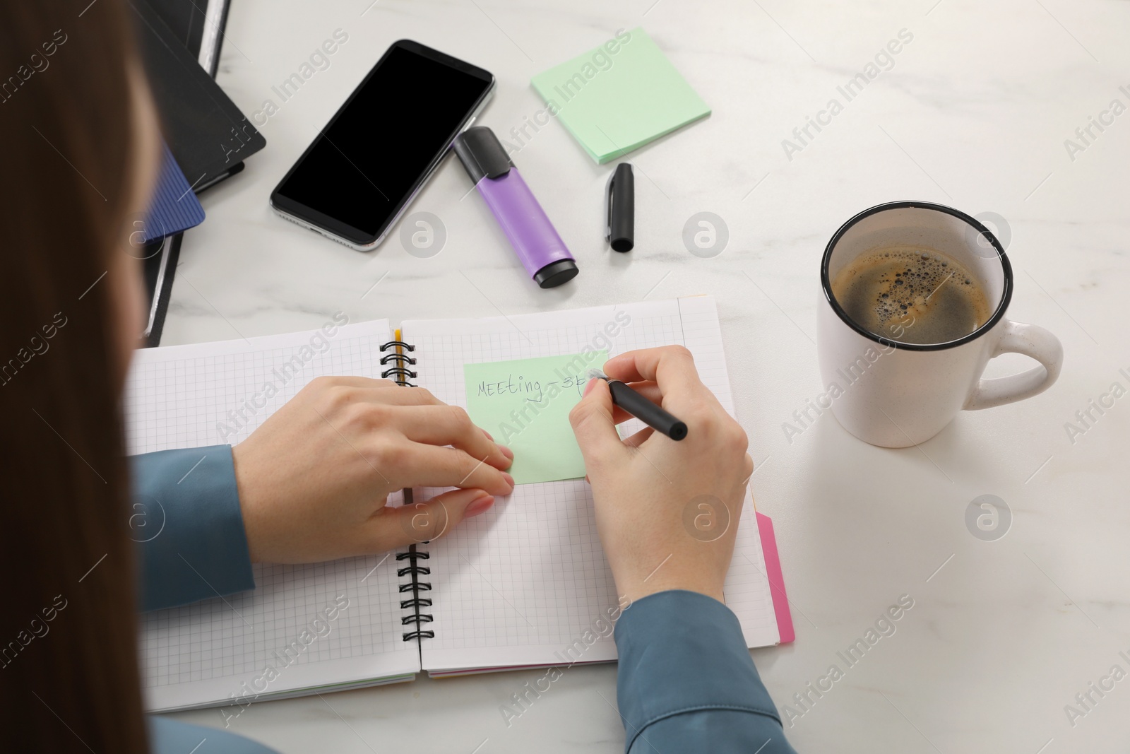 Photo of Woman writing on sticky note at white marble table, closeup