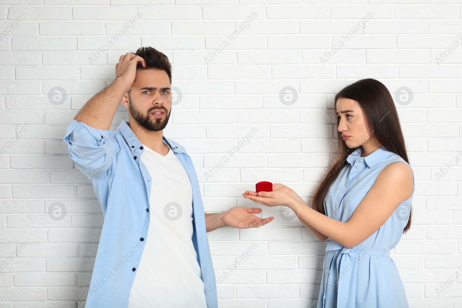 Photo of Young woman with engagement ring making marriage proposal to her boyfriend near white brick wall