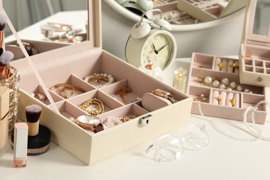 Photo of Jewelry boxes with many different accessories, perfumes and alarm clock on white table