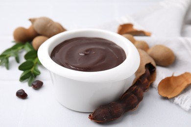 Photo of Bowl of tasty tamarind sauce and fresh pods on white table, closeup