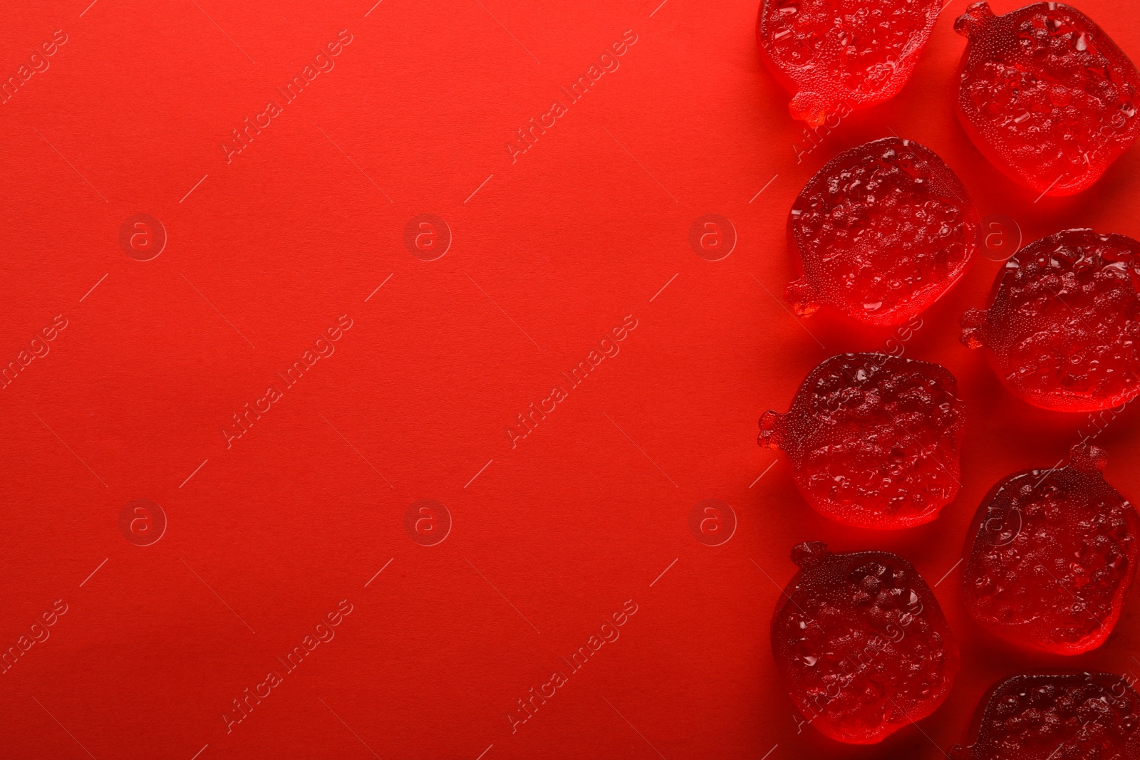 Photo of Delicious gummy pomegranate candies on red background, flat lay. Space for text