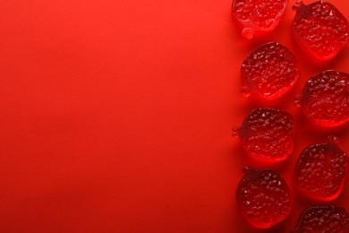 Photo of Delicious gummy pomegranate candies on red background, flat lay. Space for text