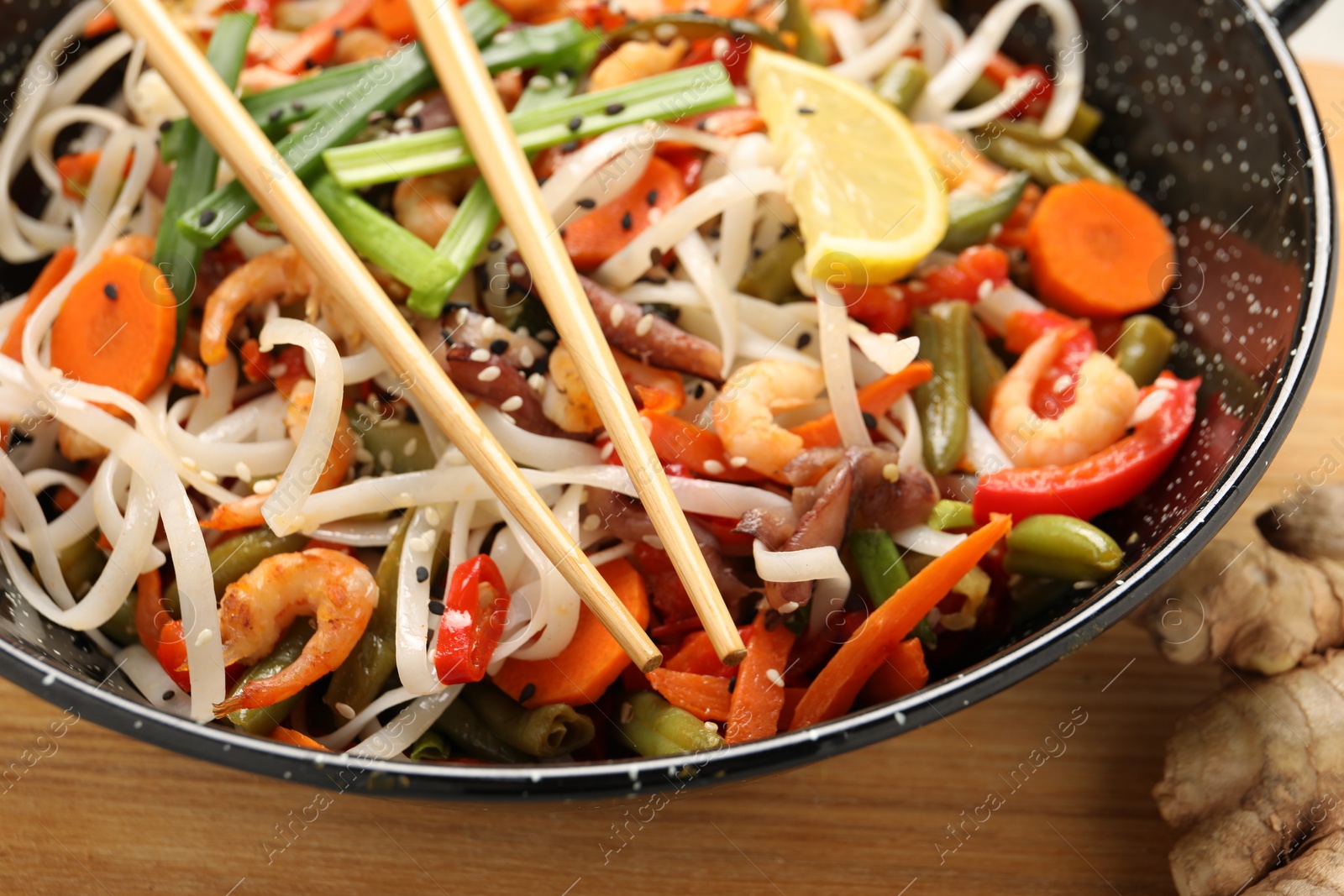 Photo of Shrimp stir fry with noodles and vegetables in wok on wooden table, closeup