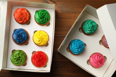 Boxes with delicious colorful cupcakes on wooden table, flat lay