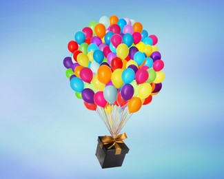 Many balloons tied to gift box on bright background