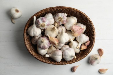 Photo of Fresh organic garlic in wicker basket on white wooden table, flat lay