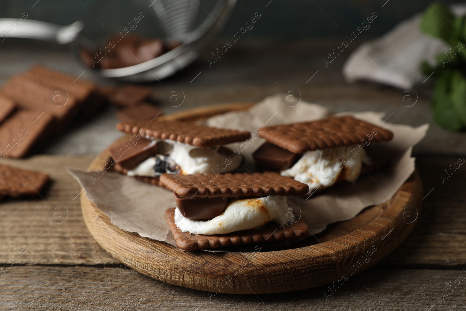 Photo of Delicious marshmallow sandwiches with crackers and chocolate on wooden table, closeup