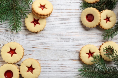 Photo of Traditional Christmas Linzer cookies with sweet jam and fir branches on wooden background
