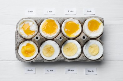 Different cooking time and readiness stages of boiled chicken eggs on white wooden table, flat lay