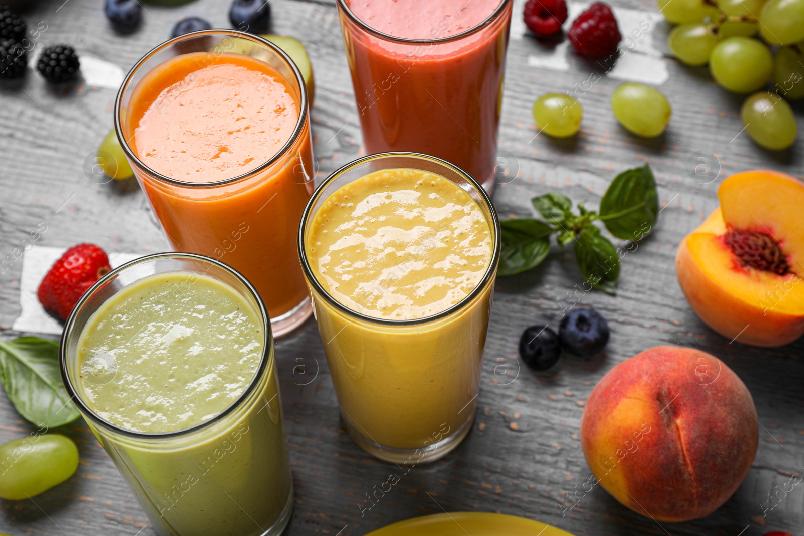 Photo of Many different delicious smoothies and ingredients on grey wooden table