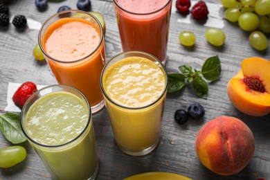 Many different delicious smoothies and ingredients on grey wooden table