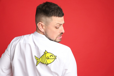 Photo of Man with paper fish on back against red background. April fool's day