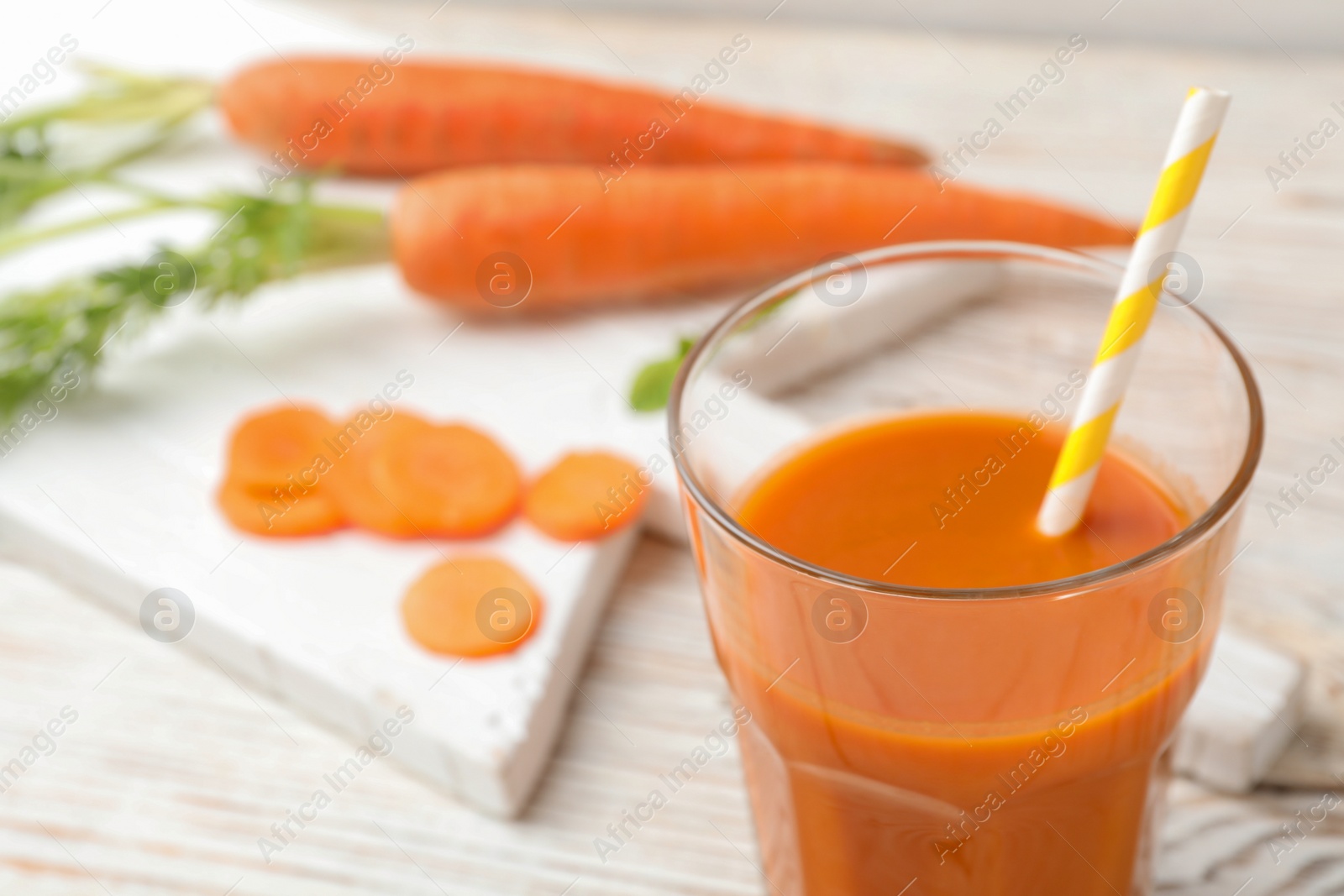 Photo of Glass of fresh carrot juice on white wooden table, space for text