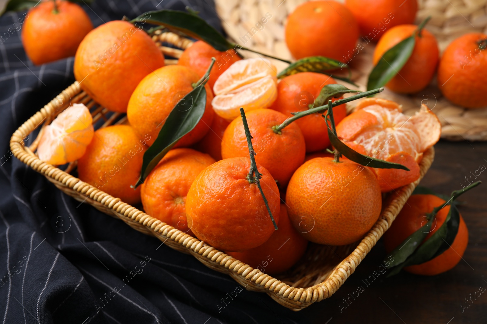 Photo of Fresh ripe tangerines with green leaves in wicker basket on wooden table, closeup