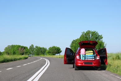 Family car with open trunk full of luggage on highway. Space for text