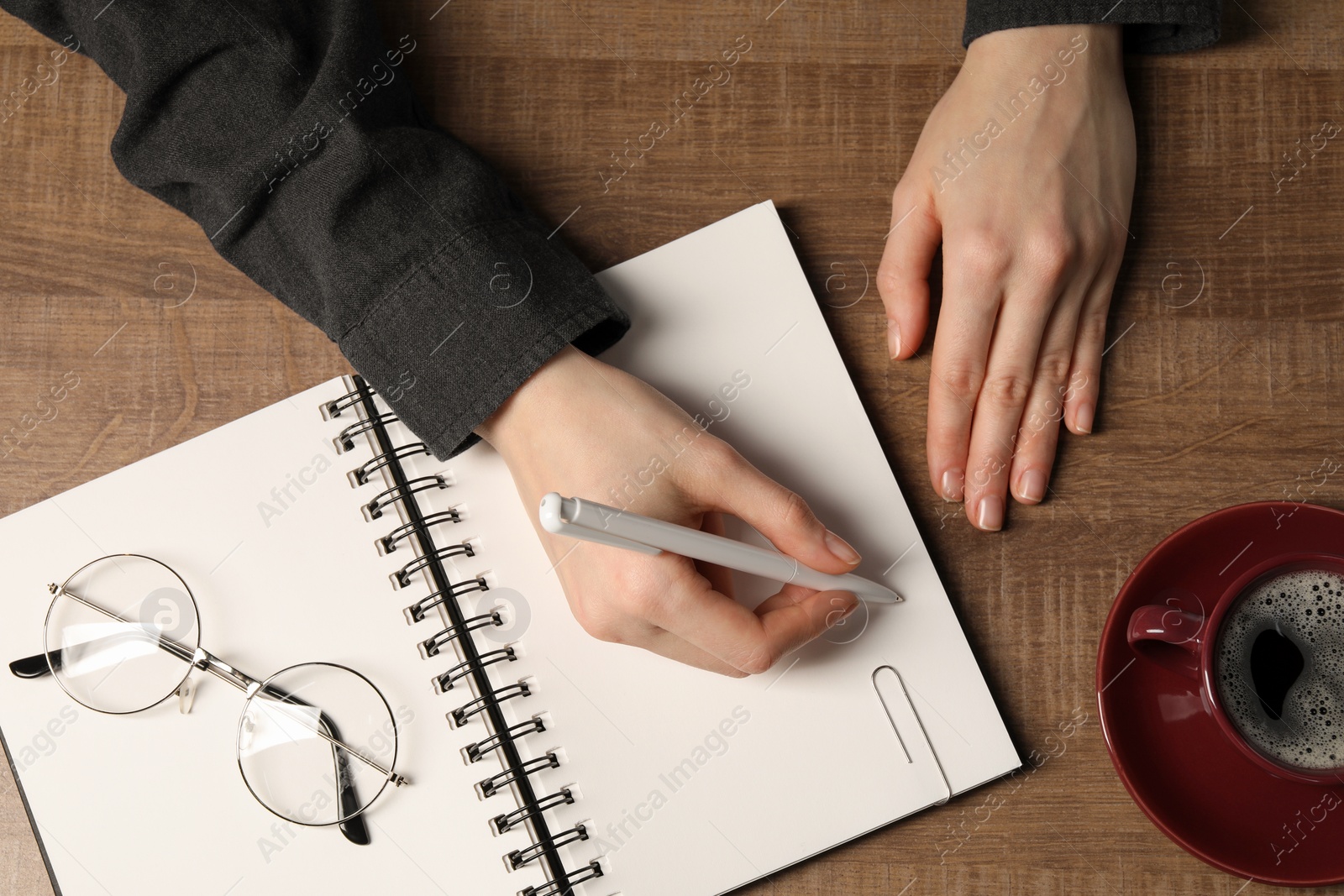 Photo of Woman writing in notebook at wooden table, top view