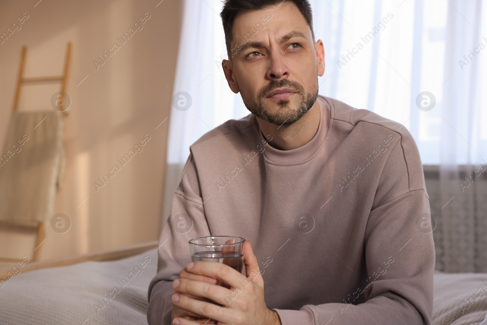 Photo of Upset man with glass of water in bedroom. Loneliness concept