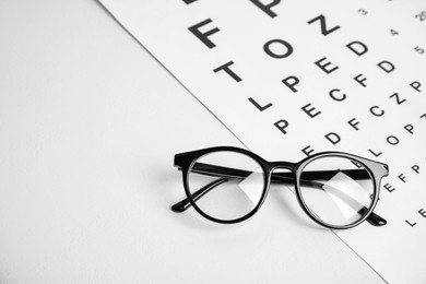 Photo of Glasses and eye chart test on white table, space for text. Ophthalmologist tools