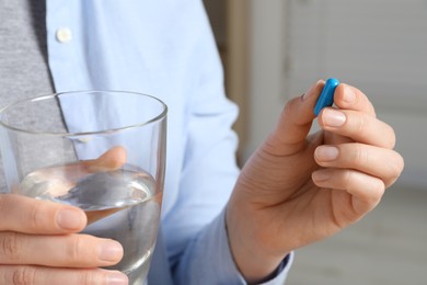 Woman with pill and glass of water on blurred background, closeup