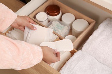 Photo of Young woman taking menstrual pad and pantyliner out of drawer, closeup