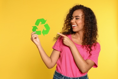 Photo of Young African-American woman with recycling symbol on yellow background