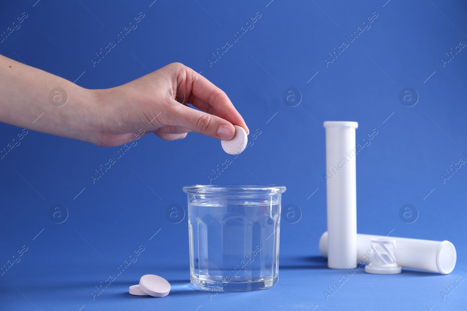 Photo of Woman putting effervescent pill into glass of water on blue background, closeup