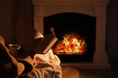 Photo of Woman with book and cup near fireplace indoors, closeup. Cozy atmosphere