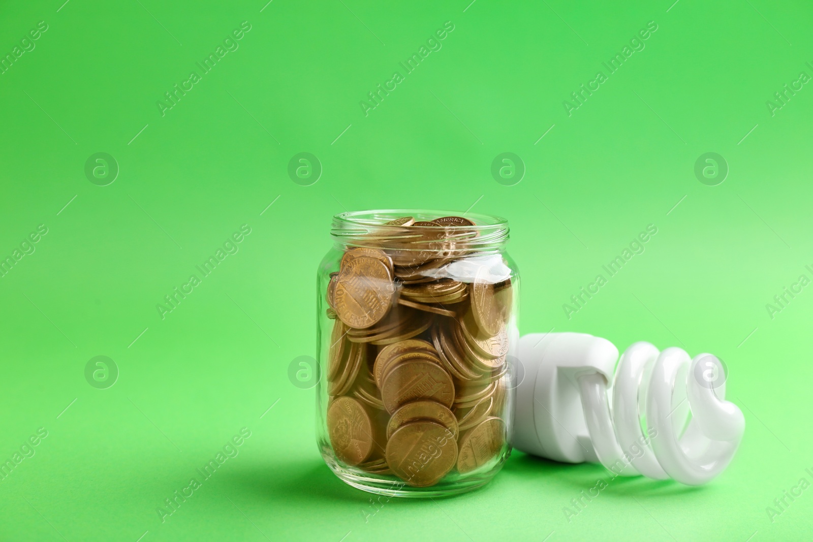 Photo of Glass jar with coins and light bulb on color background. Space for text