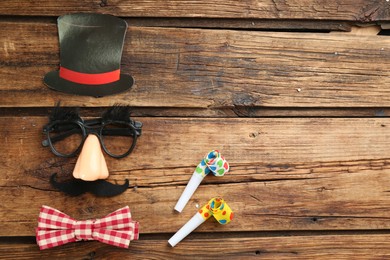 Photo of Flat lay composition with clown face made of mask, cylinder and bow tie on wooden table. Space for text