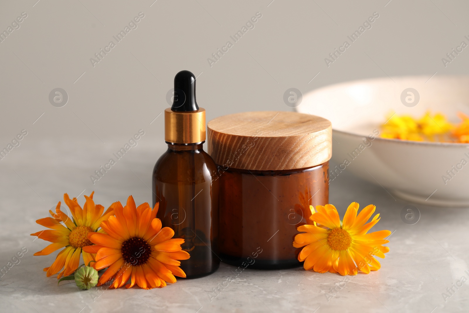 Photo of Bottle and jar of cosmetic products with beautiful calendula flowers on light grey marble table