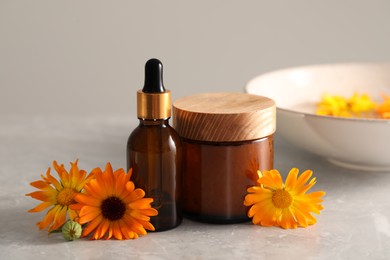 Bottle and jar of cosmetic products with beautiful calendula flowers on light grey marble table