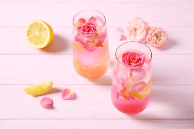 Photo of Delicious refreshing drink with lemon and roses on pink wooden table