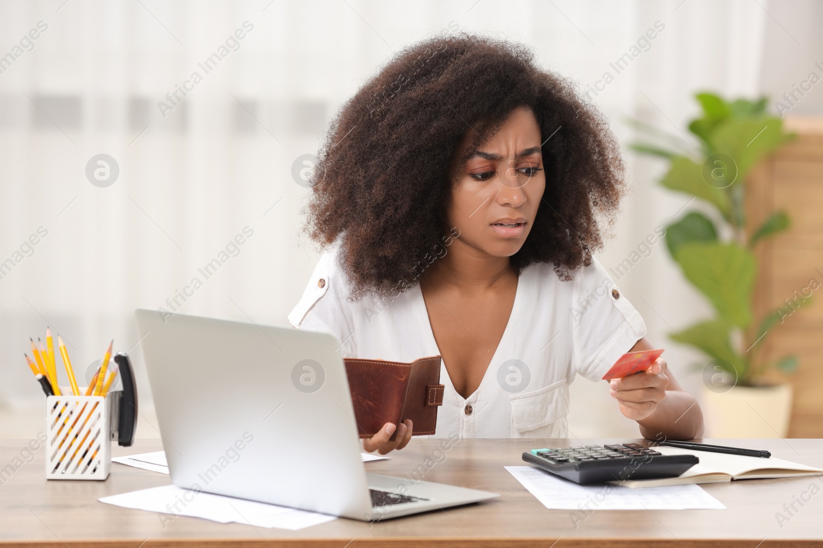 Photo of Confused woman with credit card and wallet planning budget at table in room. Debt problem