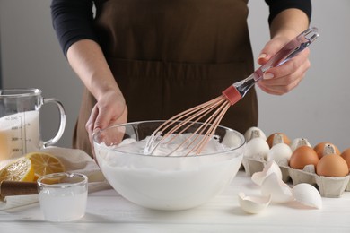 Photo of Woman making whipped cream with whisk at white wooden table, closeup