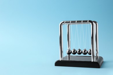 Photo of Newton's cradle on light blue background, space for text. Physics law of energy conservation