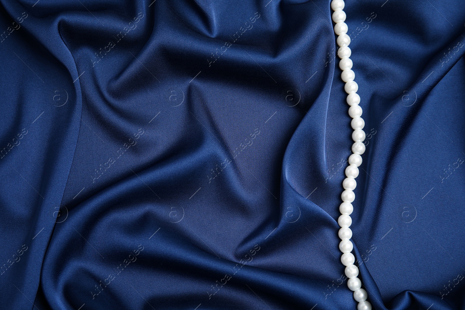 Photo of Beautiful pearls on dark blue silk, top view. Space for text