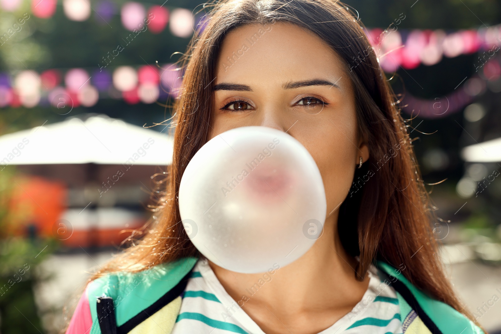 Photo of Beautiful young woman blowing chewing gum on city street outdoors