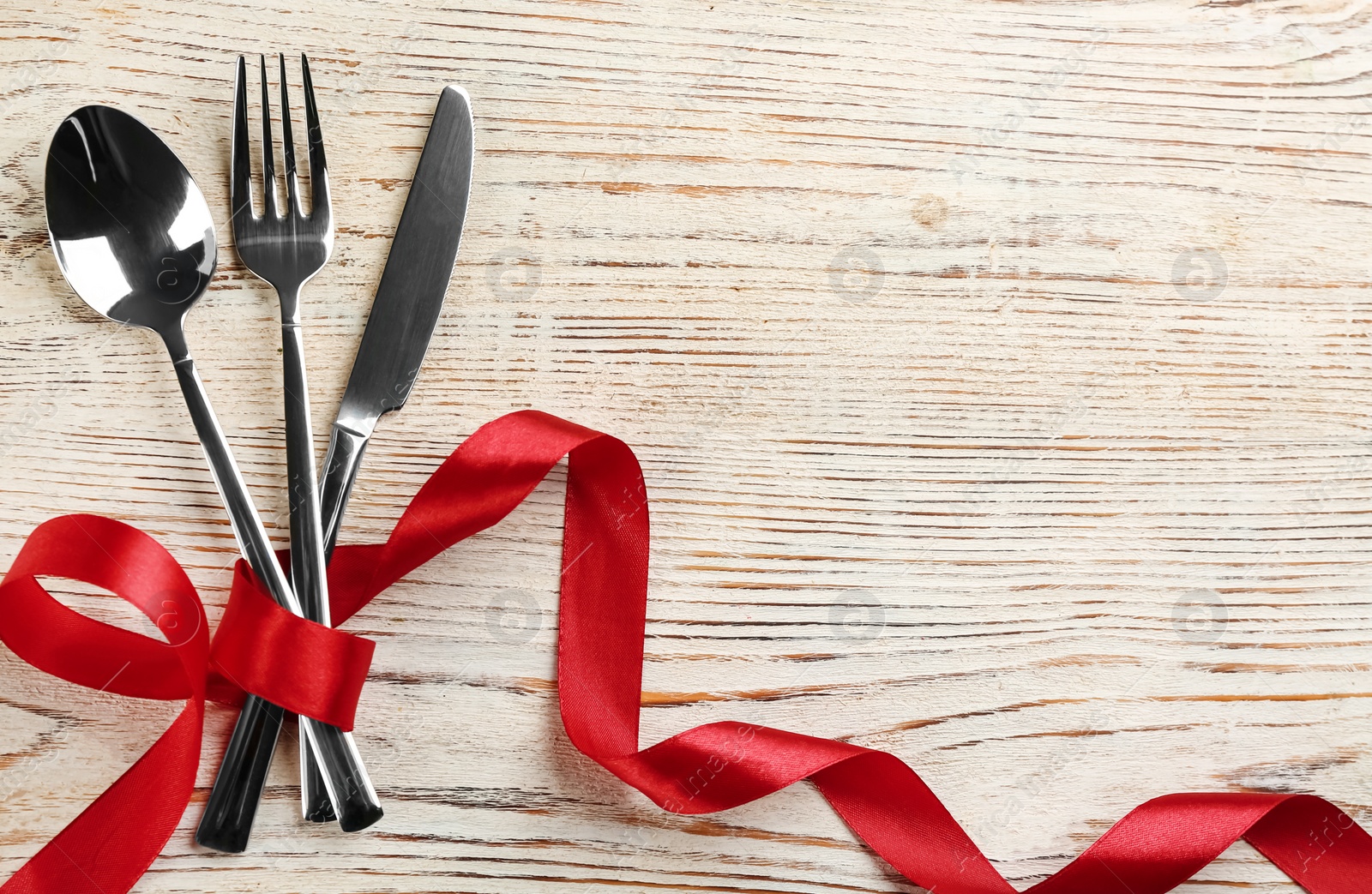 Photo of Cutlery set and red ribbon on white wooden  background, flat lay with space for text. Valentine's Day dinner